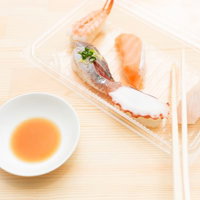 透明な容器に入った4種の握り寿司と醤油と箸の写真