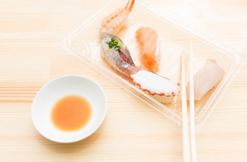 透明な容器に入った4種の握り寿司と醤油と箸