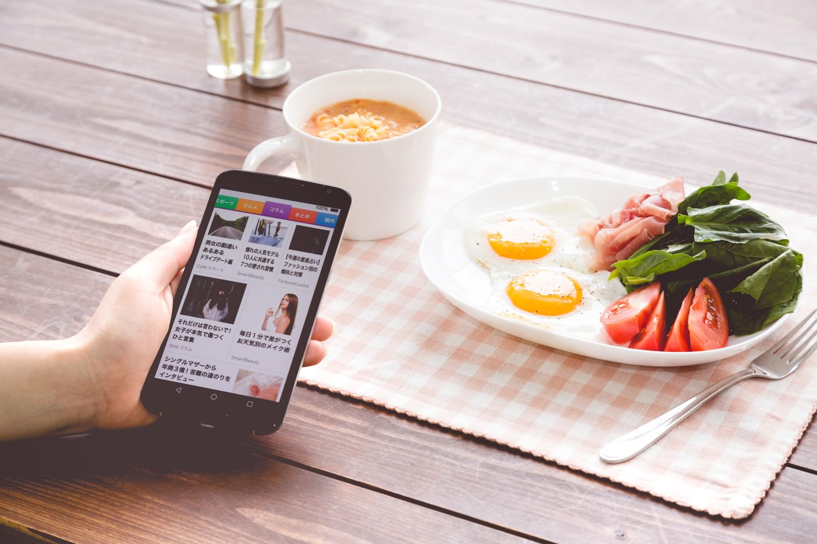 朝食の食卓でスマートニュースアプリをチェックする女性の手