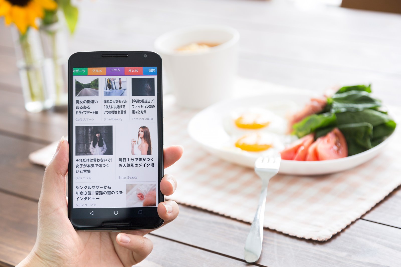 朝食テーブルでスマートフォンを持ってニュースをチェックする女性
