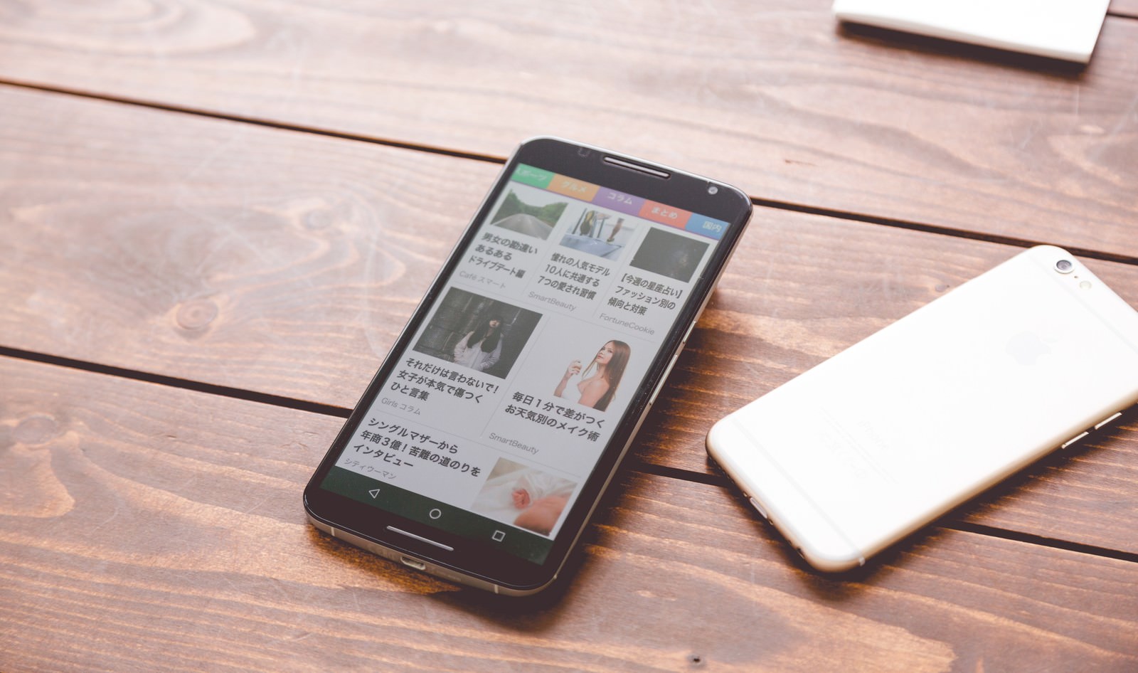 黒と白のスマートフォンが木製デスクに並んでニュースアプリを表示