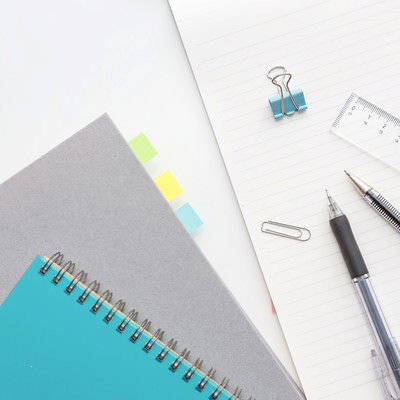 白い机に並んだノートと筆記用具の俯瞰の写真