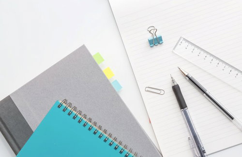 白い机に並んだノートと筆記用具の俯瞰
