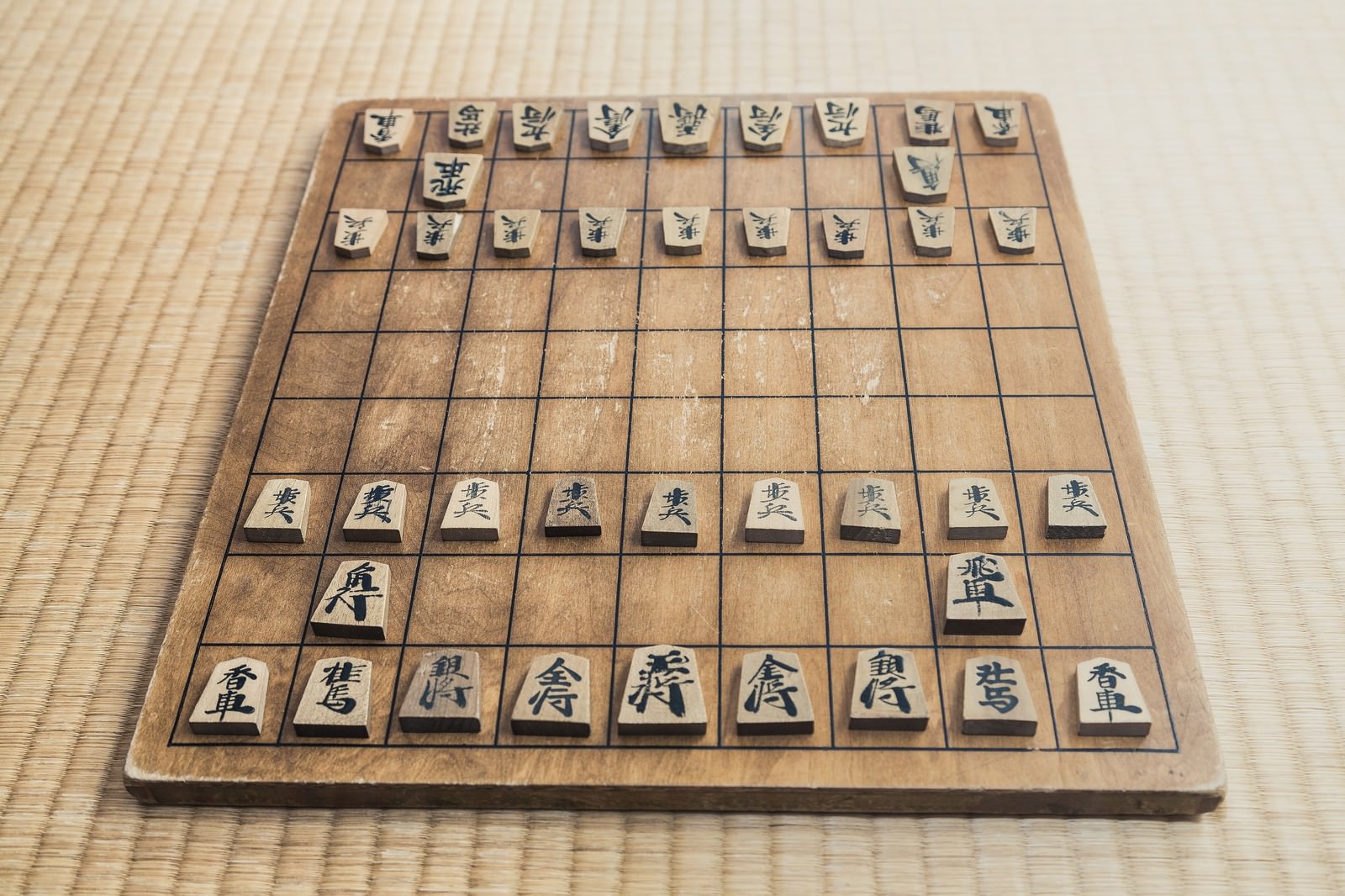 畳の上に初期配置で置かれた将棋盤と木製の駒