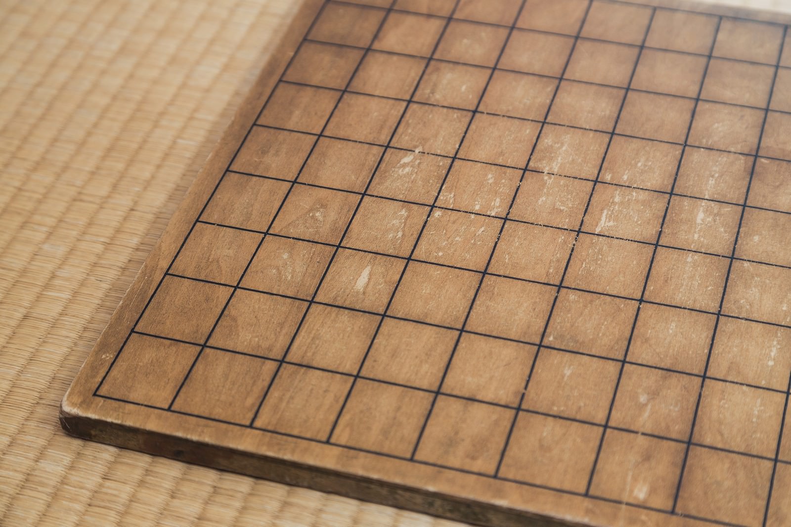 古い木製の将棋盤。黒い線で升目が引かれた盤面が斜め上から撮影されている