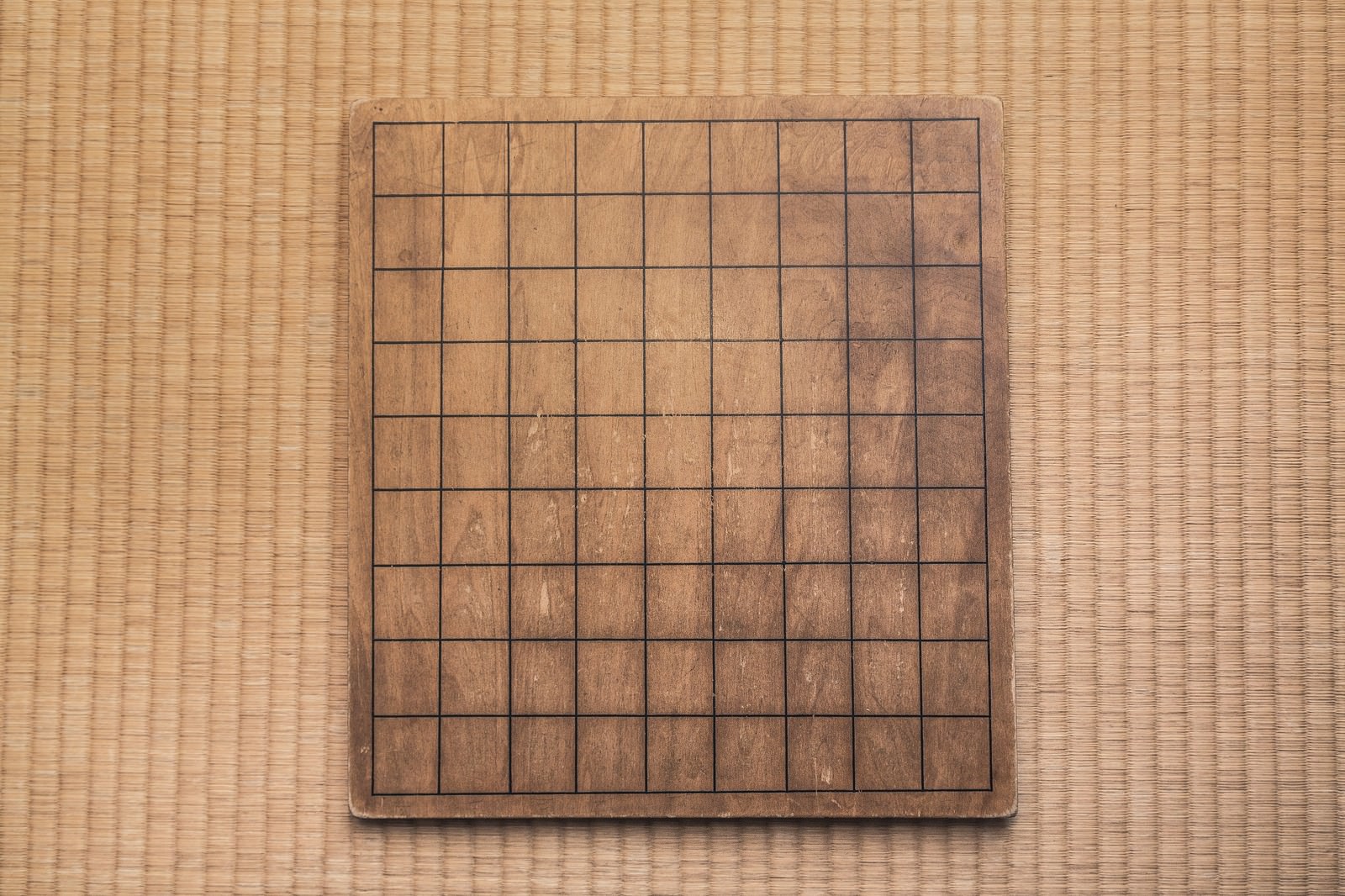 茶色い木製の将棋盤。黒い線で正方形にマス目が引かれている。