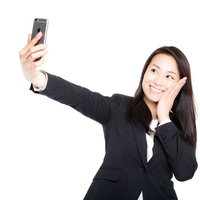 スマートフォンで自撮りしながら歯痛ポーズを決める女性社員の写真