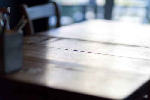 木製のテーブルに広げた書類とペン、照明とペンケースのある作業スペースの写真