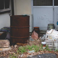 錆びたドラム缶と不法投棄されたごみ、廃墟に散乱する廃棄物の写真