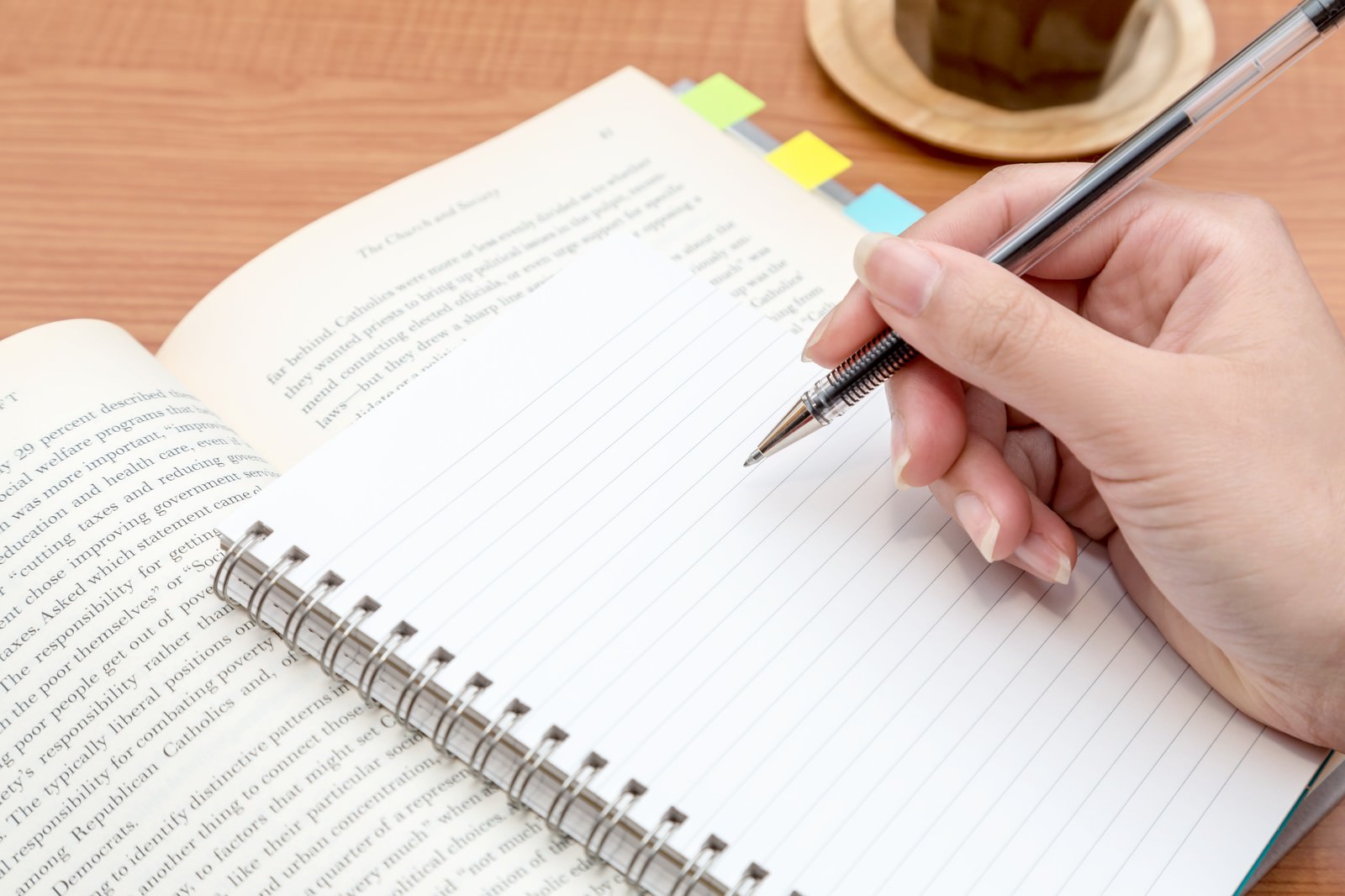 カラフルな付箋が貼られたリングノートにシャープペンシルで書き込もうとしている手元