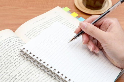 付箋を貼ったノートにペンで書き込む手元