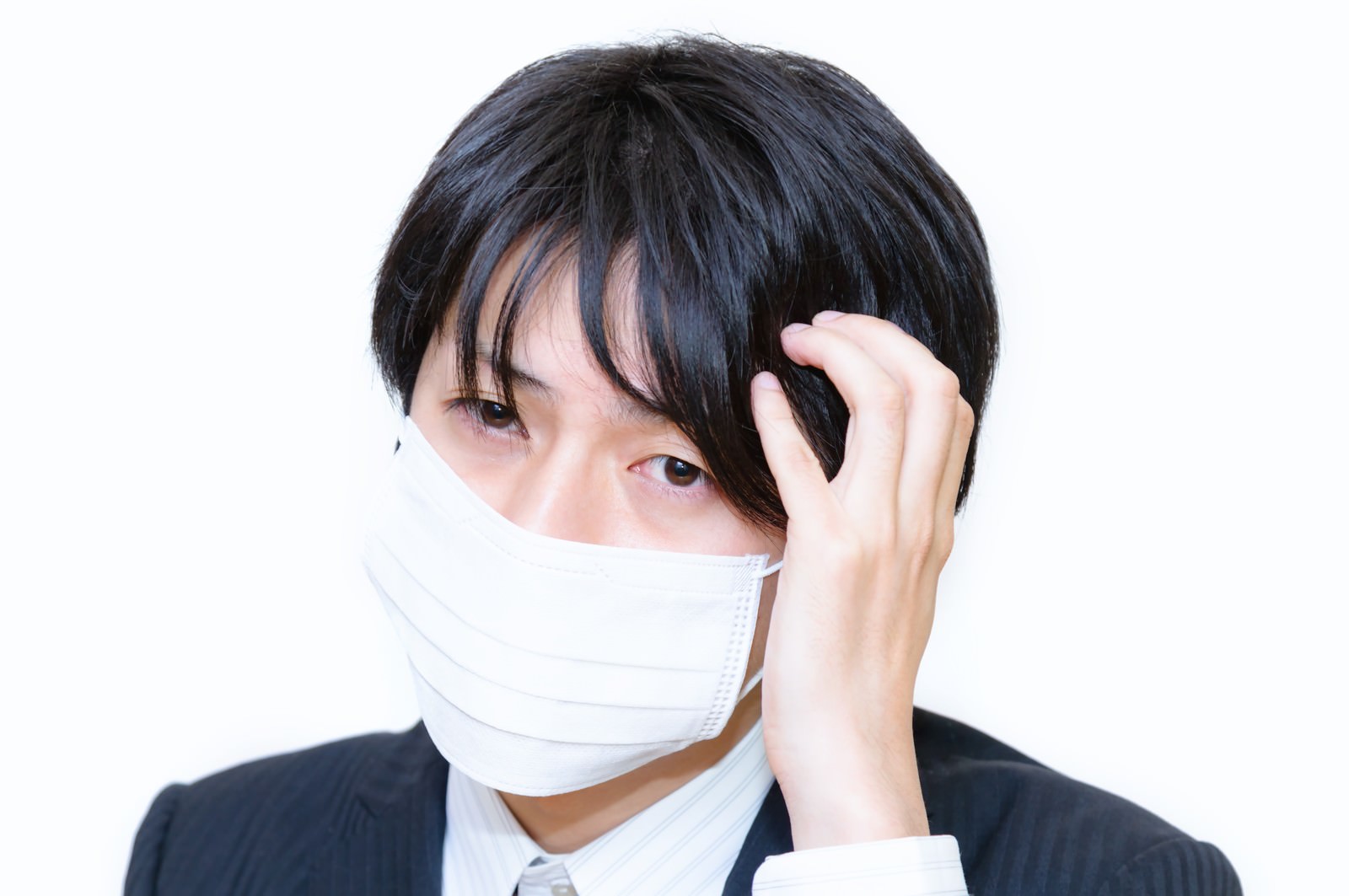 マスクをした男性がこめかみを押さえて頭痛の症状を見せている［モデル：Tsuyoshi.］