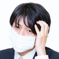 マスクをして頭に手を当てるスーツの男性の写真