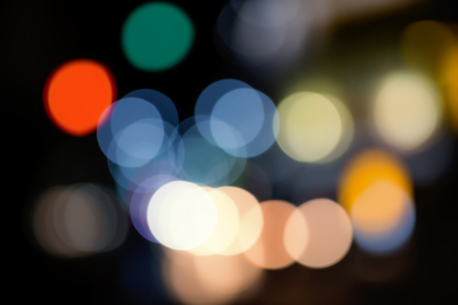 街の光がボケて浮かぶ夜景。オレンジ、青、白の光点が円形に重なっている