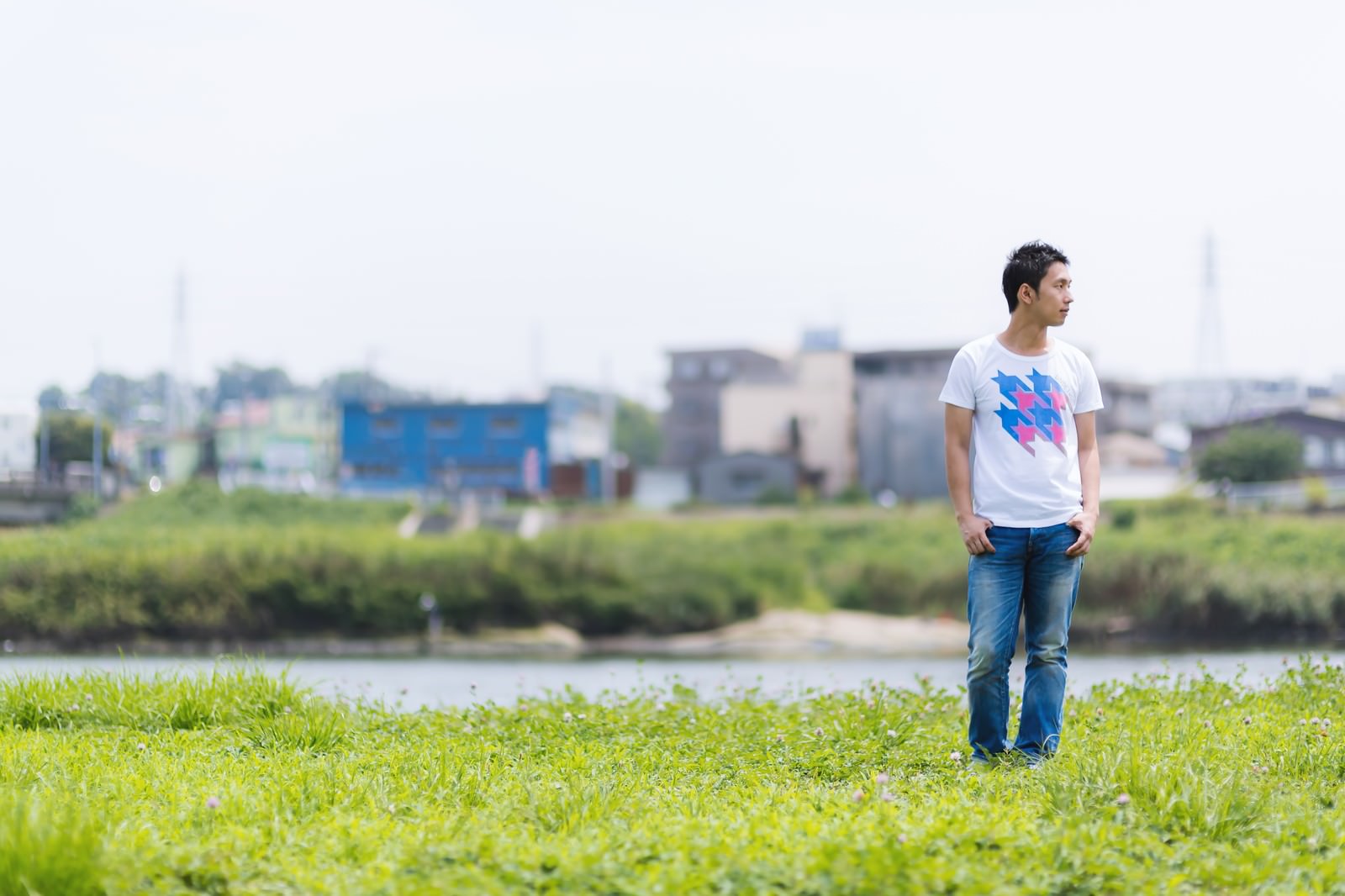 河川敷に立って遠くを見つめる白いTシャツの男性［モデル：大川竜弥］