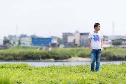 河川敷の草の上に立つ白Tシャツの男性