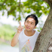 木の陰から指を差す白Tシャツの男性の写真