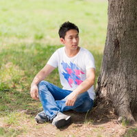 公園の木陰でくつろぐ若い男性の写真