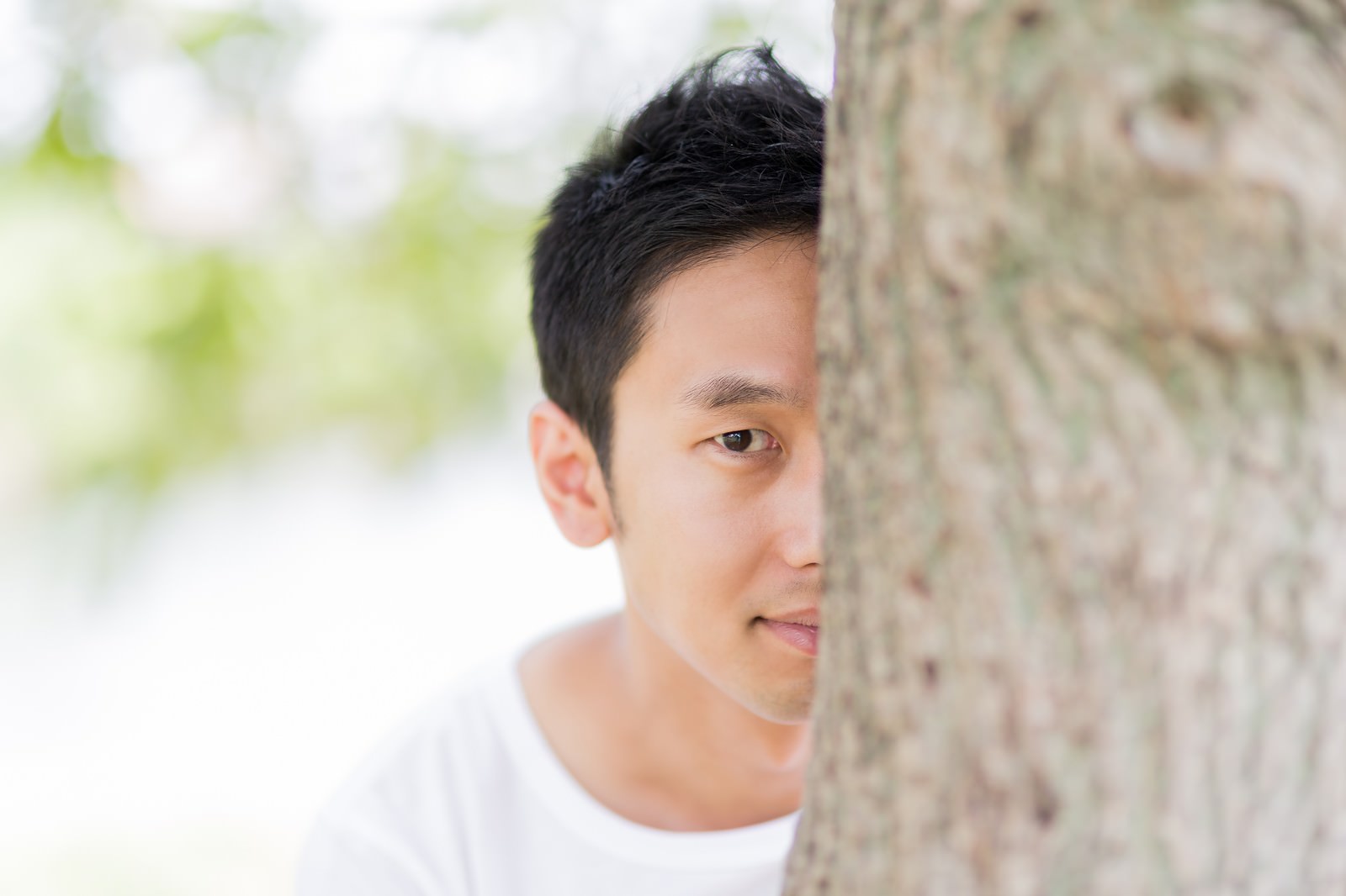 木陰から顔を出して見つめる男性の横顔アップ［モデル：大川竜弥］