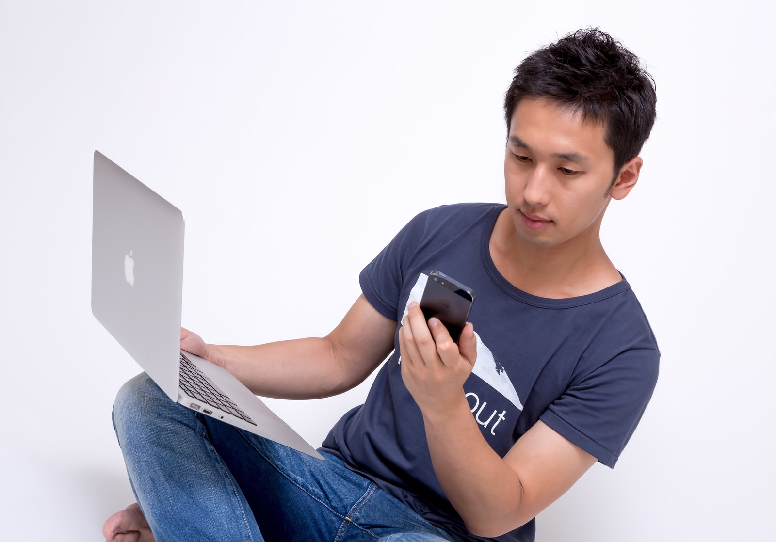 MacBook ProとiPhoneを同時に持つ若い男性が、スマートフォンを確認している［モデル：大川竜弥］