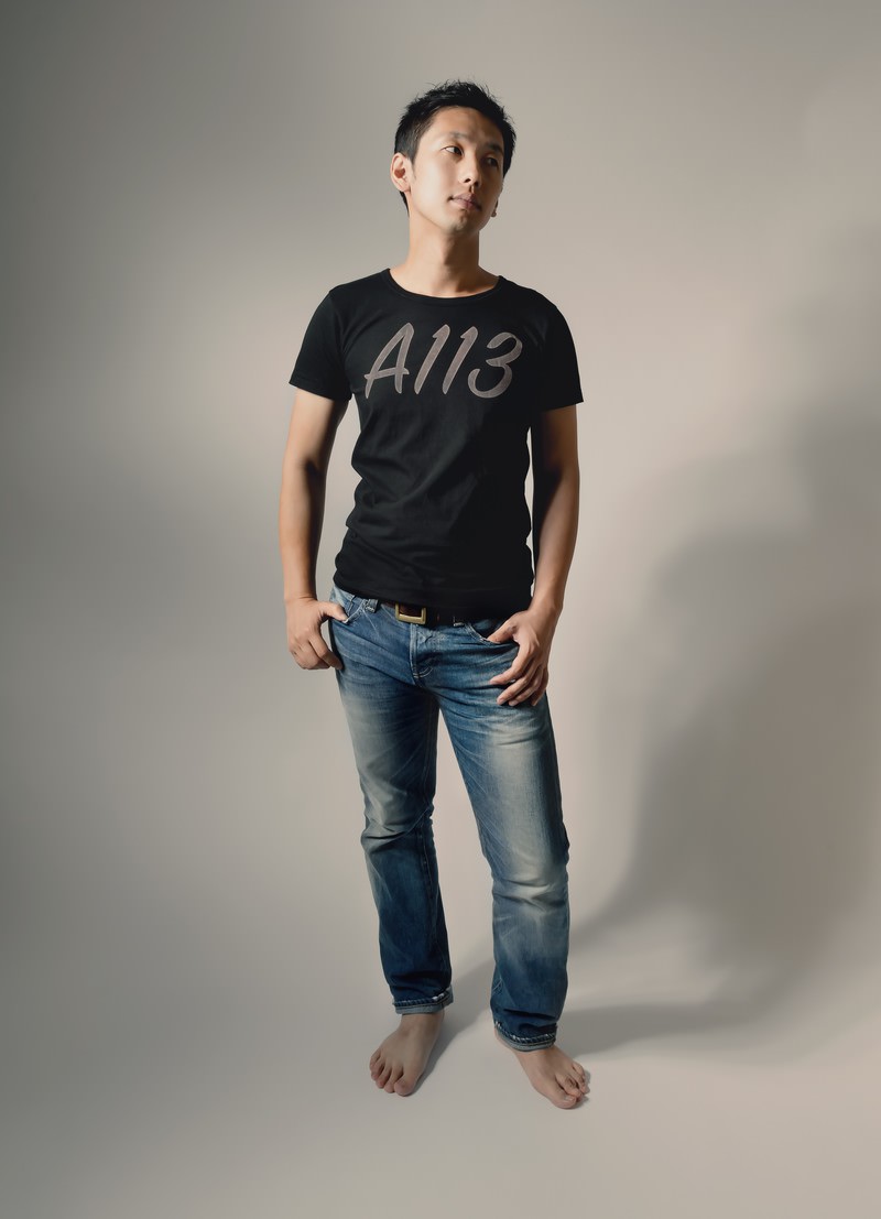 A113と書かれた黒いTシャツを着た男性が上を向いてポージングしている［モデル：大川竜弥］
