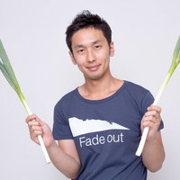 両手にネギを持つ紺Tシャツの男性の写真