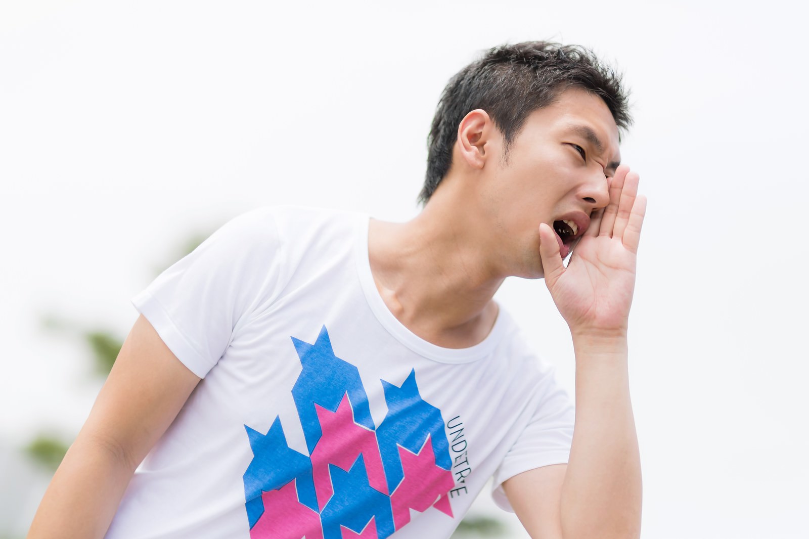 白いTシャツを着た男性が手を口に当てておもいっきり叫んでいる［モデル：大川竜弥］