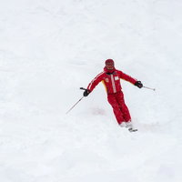 雪の斜面を赤いウェアで滑るスキーヤーの写真