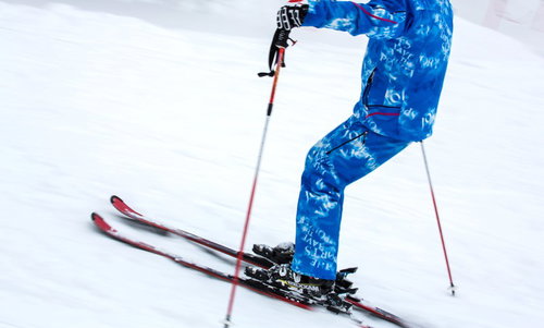 スキー板とポールで雪の斜面を滑るスキーヤーの足元