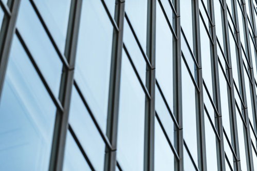 オフィスビルの格子状に並ぶガラス窓と青空の反射