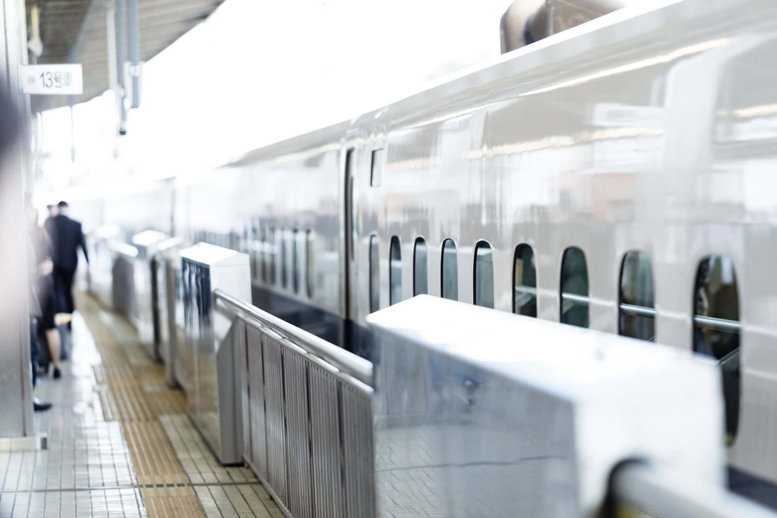 ホームに停車している白い新幹線と歩く乗客たち