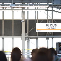 新大阪駅のホームの駅名標と構内を行き交う人々の写真