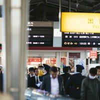 新幹線ホームの人混みと発車時刻案内板を見上げる乗客の写真