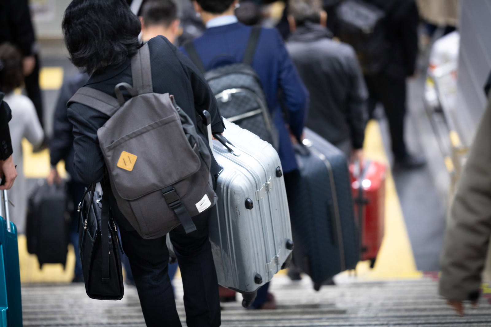 重いスーツケースを手に持って階段を下りる人の後ろ姿