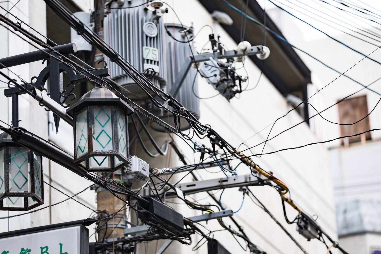 繁華街に立つ電柱と複数の電線が張り巡らされた都市の街並み