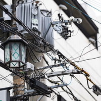 繁華街に立つ電柱と複数の電線が張り巡らされた街並みの写真