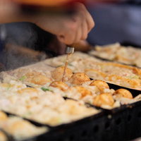 露天の出店で焼く、アツアツのたこ焼きの写真