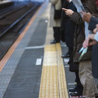 駅ホームでマスクをして新聞を読む女性の写真