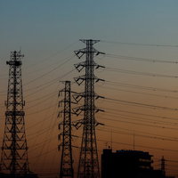 朝焼け空にシルエットで並ぶ送電鉄塔と電線の写真