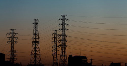 朝焼け空にシルエットで並ぶ送電鉄塔と電線