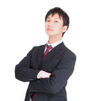 腕を組んで上を見上げるスーツ姿のビジネスマンの写真