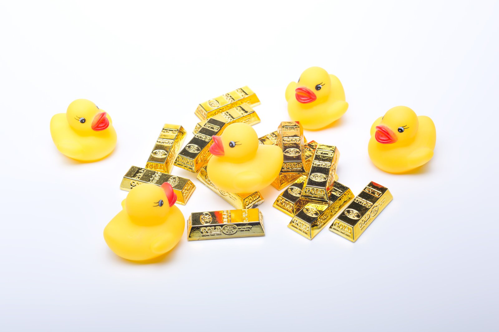 黄色いアヒルおもちゃ5体が金色の金塊おもちゃに囲まれている配置