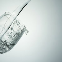 傾いたワイングラスから溢れ出す水の写真