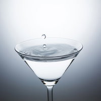 カクテルグラスに落ちる水滴と波紋の写真