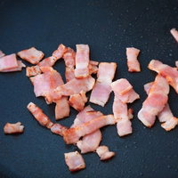 黒いフライパンで油に散らばるカリカリのベーコンの写真