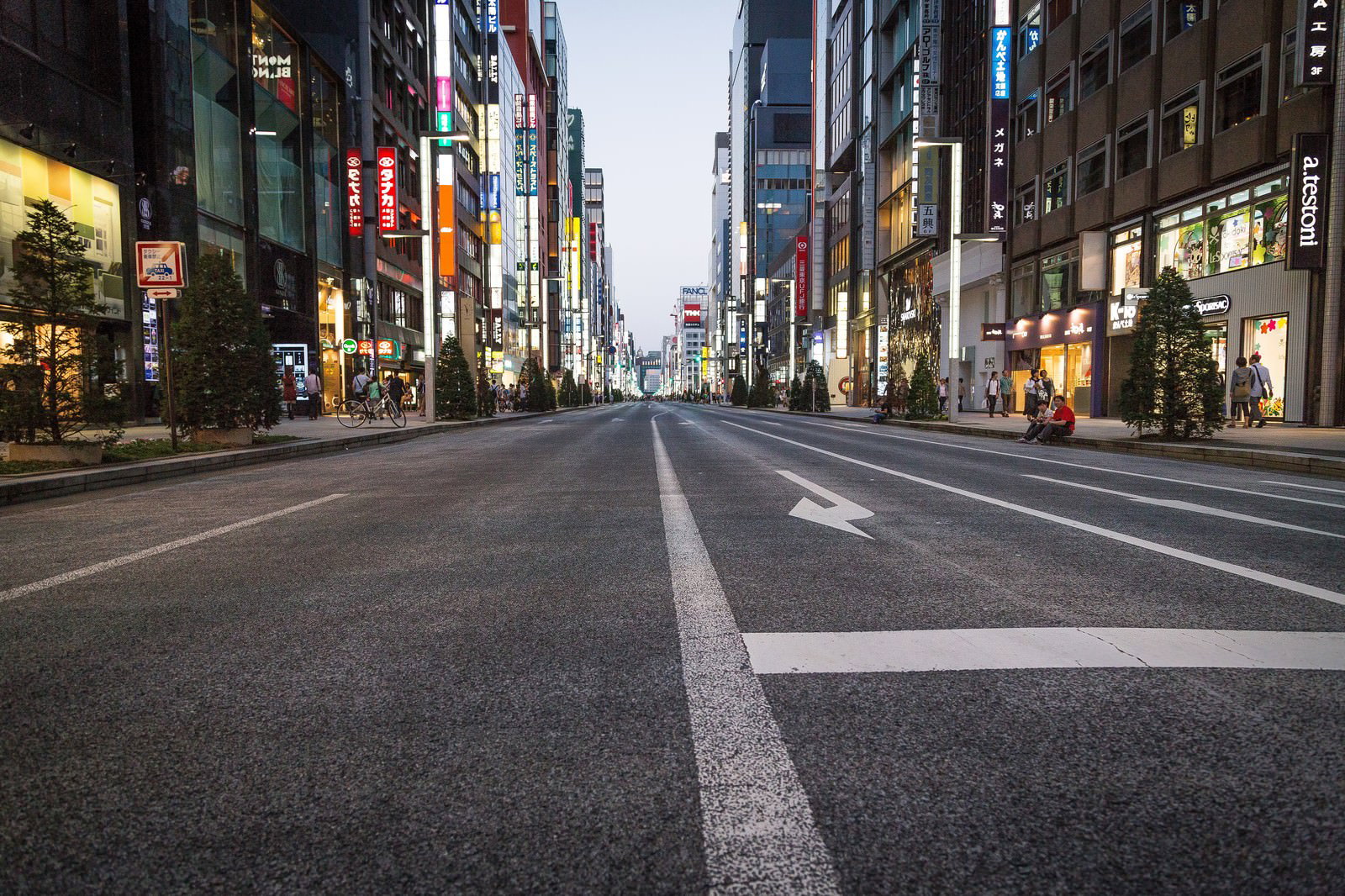 銀座の歩行者天国を撮影した夕方の街並み。両側の高層ビルにネオン看板が灯り、道路には白い標識が引かれている