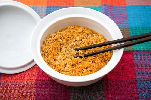 カラフルな織物の上でオレンジ色の麺に箸を置いたチキンラーメン