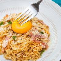 フォークに刺さった卵黄が中央にのるカルボナーラ風汁なしラーメンの写真