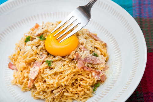 フォークに刺さった卵黄が中央にのるカルボナーラ風汁なしラーメン