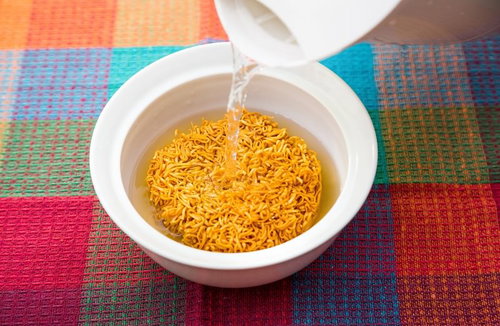 格子模様の布の上で白い容器の麺に熱湯を注ぐ瞬間